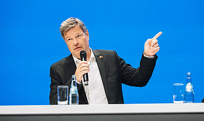 Portraitbild von Bundeswirtschaftsminister Dr. Robert Habeck, der auf einer Podiumsbühne steht und in ein Mikrofon spricht.