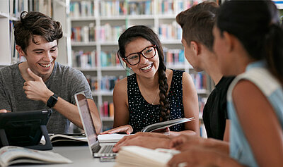 Gruppe von männlichen und weiblichen Studierenden sitzt in der Bibliothek und lacht