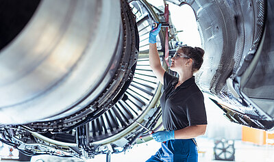 Eine junge Mechanikerin prüft eine Flugzeugturbine.