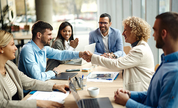 Handschlag im Büro zwischen einem jungen Mann und einer älteren Frau