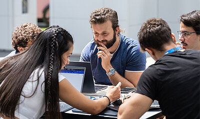 Eine Gruppe an jungen Menschen sitzen vor ihrem Laptops während eines Hackatons.