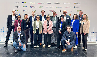 Ein Gruppenbild mit 15 Personen die auf der Hannover Messe vor einer Projektwand stehen.